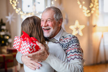Porträt einer jungen Frau, die ihrem glücklichen Großvater zu Hause zu Weihnachten ein Geschenk überreicht. - HPIF22237