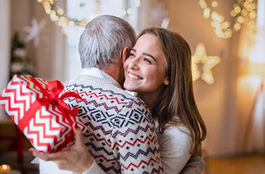 Porträt einer jungen Frau, die ihrem glücklichen Großvater zu Hause zu Weihnachten ein Geschenk überreicht. - HPIF22238