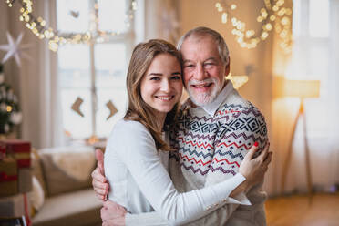 Lachender älterer Mann mit junger Frau in einem Haus zu Weihnachten, die sich umarmen. - HPIF22241