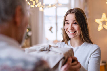 Überrumpelte junge Frau, die ein Weihnachtsgeschenk von ihrem nicht erkennbaren Großvater zu Hause entgegennimmt. - HPIF22245