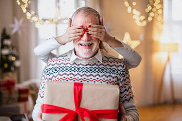 Unerkennbare junge Frau, die ihrem älteren Großvater zu Hause zu Weihnachten ein Geschenk überreicht, Mittelteil. - HPIF22248