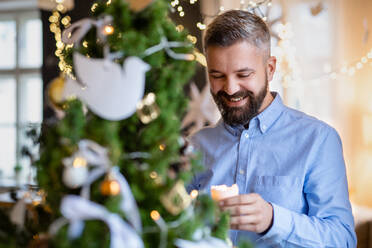 Porträt eines reifen Mannes, der zu Weihnachten zu Hause ist und eine Kerze hält. - HPIF22253