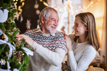 Glückliche junge Frau mit älterem Großvater zu Hause beim Weihnachtsbaumschmücken. - HPIF22256