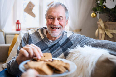 Portrait of happy senior man indoors at home at Christmas, eating biscuits. - HPIF22257