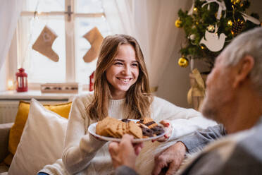 Porträt einer jungen Frau mit ihrem Großvater zu Hause an Weihnachten, die Kekse essen. - HPIF22258