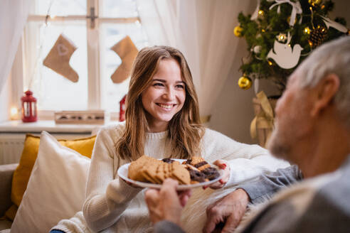 Portrait of young woman with grandfather indoors at home at Christmas, eating biscuits. - HPIF22258