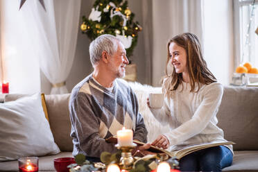 Porträt einer jungen Frau mit ihrem Großvater, die zu Weihnachten zu Hause in einem Fotoalbum blättert. - HPIF22265