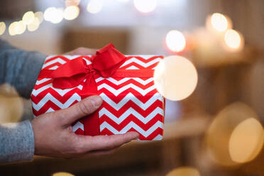 Nahaufnahme der Hände eines nicht erkennbaren reifen Mannes, der zu Hause an Weihnachten ein Geschenk hält. - HPIF22280
