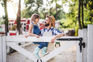 Ein Porträt des Vaters mit seiner kleinen Tochter auf dem Bauernhof der Familie, stehend vor einem Holztor. - HPIF22290