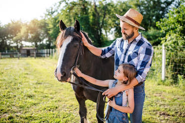 Ein reifer Vater und eine kleine Tochter mit Pferd arbeiten auf einem kleinen Familienbauernhof. - HPIF22316