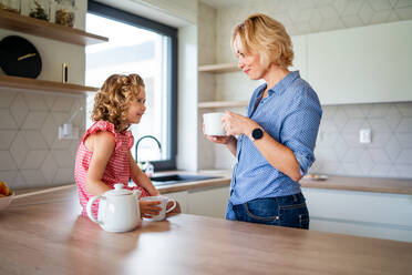 Ein glückliches süßes kleines Mädchen mit Mutter drinnen in der Küche zu Hause, Tee trinken. - HPIF22349