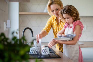 Ein niedliches kleines Mädchen mit seiner Mutter in der Küche zu Hause, beim Abwasch des Geschirrs. - HPIF22355