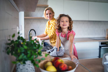 Ein niedliches kleines Mädchen mit seiner Mutter in der Küche zu Hause, beim Abwasch des Geschirrs. - HPIF22357