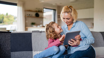 A front view of cute small girl with mother on sofa indoors at home, using tablet. - HPIF22360