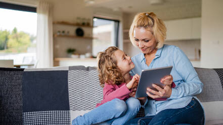 Frontansicht eines niedlichen kleinen Mädchens mit seiner Mutter auf dem Sofa zu Hause, das ein Tablet benutzt. - HPIF22360