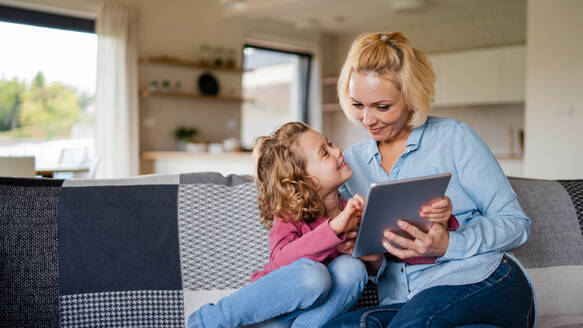 Frontansicht eines niedlichen kleinen Mädchens mit seiner Mutter auf dem Sofa zu Hause, das ein Tablet benutzt. - HPIF22360