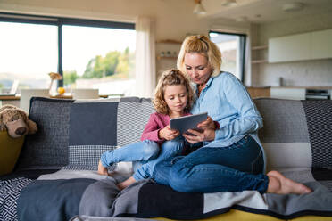 Frontansicht eines niedlichen kleinen Mädchens mit seiner Mutter auf dem Sofa zu Hause, das ein Tablet benutzt. - HPIF22361