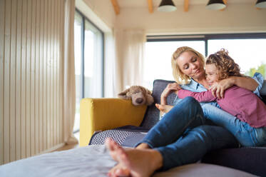 A cute small girl with mother on sofa indoors at home, resting. Copy space. - HPIF22362