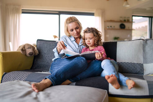 Ein süßes kleines Mädchen mit Mutter sitzt auf dem Sofa drinnen zu Hause, lesen Geschichte Buch. - HPIF22367