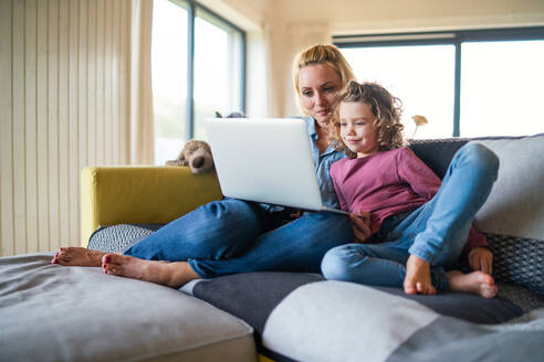 Ein süßes kleines Mädchen mit Mutter sitzt auf dem Sofa zu Hause, mit Laptop. - HPIF22371