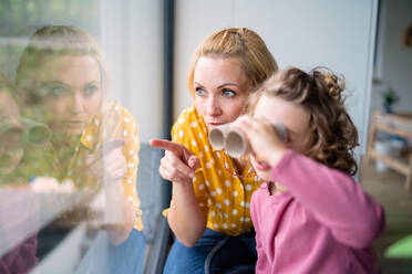 A cute small girl with mother indoors at home, playing with toy binoculars. - HPIF22411