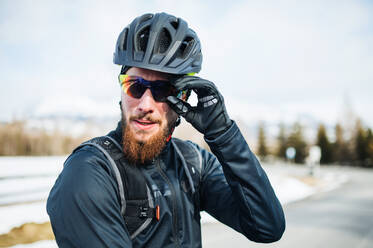 Frontansicht eines Mountainbikers mit Sonnenbrille, der im Freien in der winterlichen Natur steht. - HPIF22414