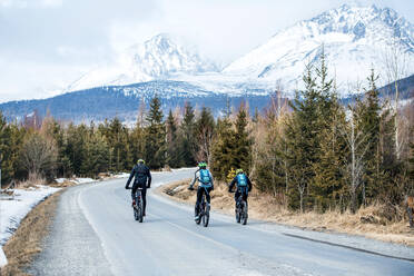 Rear view of group of mountain bikers riding on road in mountains outdoors in winter. - HPIF22423