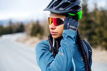 Weibliche Mountainbikerin mit Sonnenbrille steht auf der Straße im Freien im Winter. - HPIF22446