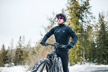 Frontansicht eines Mountainbikers mit Sonnenbrille, der im Freien in der winterlichen Natur steht. - HPIF22457