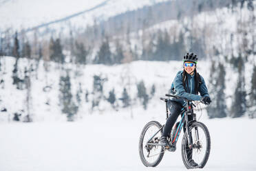 Weibliche Mountainbikerin mit Fahrrad stehend im Freien in winterlicher Natur, Raum kopieren. - HPIF22471