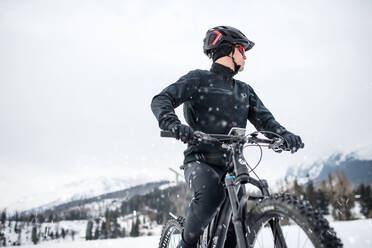 Ein Mountainbiker fährt im Schnee draußen in der winterlichen Natur und schaut weg. - HPIF22480