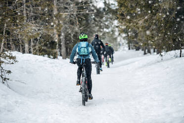 Rückansicht einer Gruppe von Mountainbikern auf einer Straße im Wald im Winter. - HPIF22497