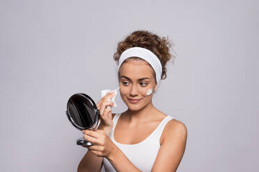 Ein Porträt einer jungen Frau, die einen Spiegel hält und ihr Gesicht in einem Studio reinigt, Schönheit und Hautpflege. - HPIF22503