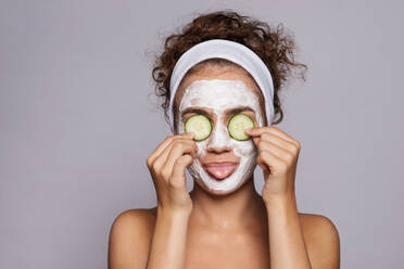 Ein Porträt einer jungen Frau mit Gesichtsmaske und Gurke in einem Studio, Schönheit und Hautpflege-Konzept. - HPIF22513