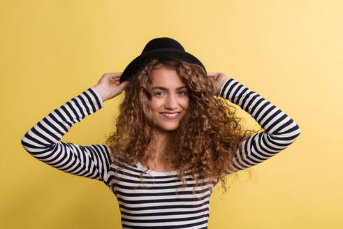 Porträt einer jungen Frau mit schwarzem Hut in einem Atelier auf gelbem Hintergrund. - HPIF22522