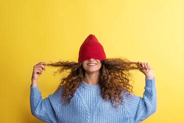 Portrait of a young woman woolen hat on her eyes in a studio on a yellow background. - HPIF22528