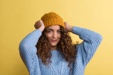 Porträt einer jungen Frau mit Wollmütze und Pullover in einem Atelier auf gelbem Hintergrund. - HPIF22529