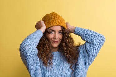 Portrait of a young woman with woolen hat and sweater in a studio on a yellow background. - HPIF22529