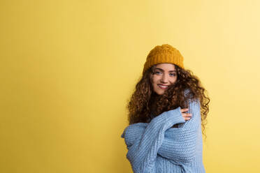 Portrait of a young woman with woolen hat and sweater in a studio on a yellow background. - HPIF22531