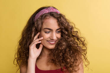 A portrait of a young woman with headband in a studio on a yellow background. - HPIF22533