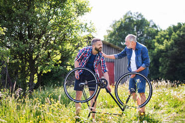 Ein erwachsener Hipster-Sohn und ein älterer Vater reparieren draußen an einem sonnigen Sommertag eine Fahrradpanne. - HPIF22539