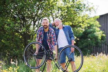 Ein erwachsener Hipster-Sohn und ein älterer Vater reparieren draußen an einem sonnigen Sommertag eine Fahrradpanne. - HPIF22540