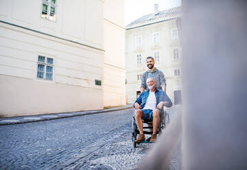 Ein erwachsener Hipster-Sohn mit seinem älteren Vater im Rollstuhl auf einem Stadtspaziergang. Platz kopieren. - HPIF22542