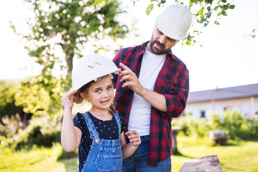 Father with a small daughter having fun with white helmets in garden. Spring nature. - HPIF22599