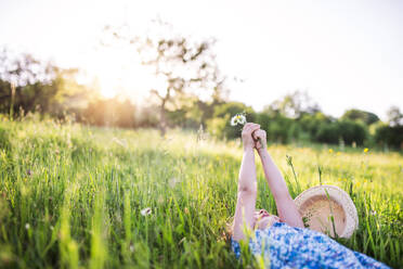 Ein kleines Mädchen, das im Frühling im Gras liegt und Blumen in der Hand hält; Kopierraum. - HPIF22608