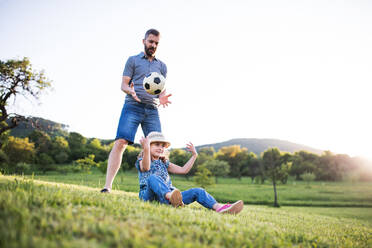 Vater mit einer kleinen Tochter, die mit einem Ball in der sonnigen Frühlingsnatur spielt. - HPIF22635