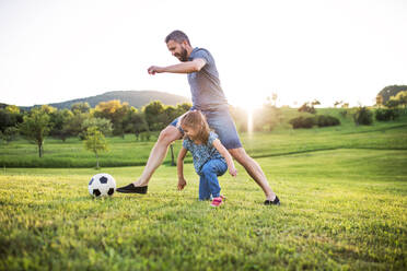 Glücklicher Vater mit einer kleinen Tochter, die mit einem Ball in der Frühlingsnatur bei Sonnenuntergang spielt. - HPIF22637