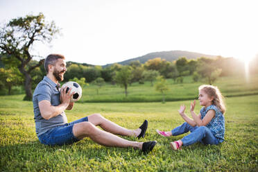 Vater mit einer kleinen Tochter, die mit einem Ball in der sonnigen Frühlingsnatur spielt. - HPIF22639