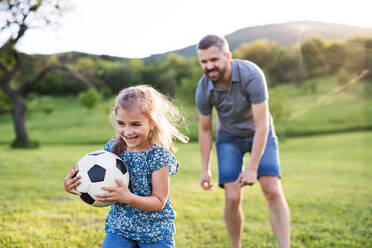 Vater mit einer kleinen Tochter, die mit einem Ball in der sonnigen Frühlingsnatur spielt. - HPIF22640