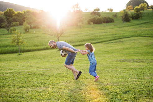 Glücklicher Vater mit einer kleinen Tochter, die mit einem Ball in der Frühlingsnatur bei Sonnenuntergang spielt. - HPIF22641